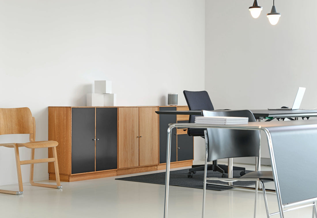 Modern office space with wooden and black filing cabinets, a desk with a laptop, and a stack of papers, under pendant lights.