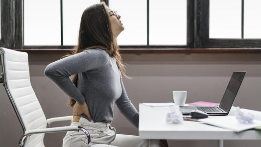 A woman sitting on a white office chair suffering from back pain due to poor sitting posture